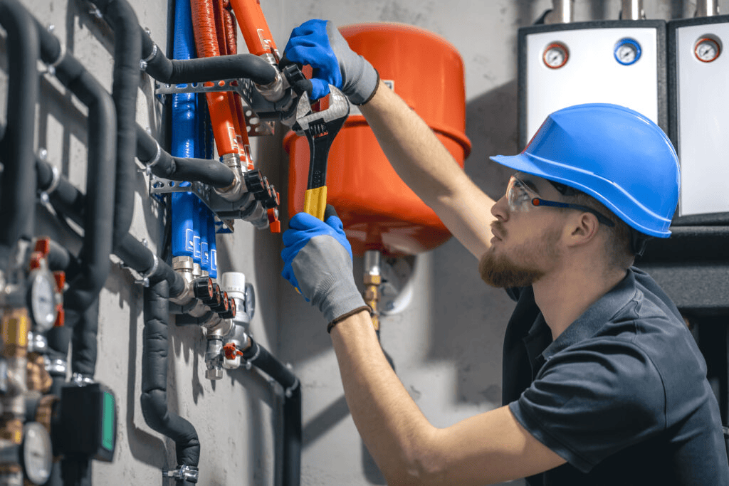 Professional HVAC technician installing residential heating system pipes and valves with adjustable wrench.