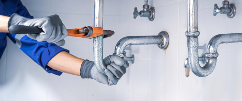 Professional plumber tightening under-sink metal drainage pipes with pipe wrench during residential plumbing repair